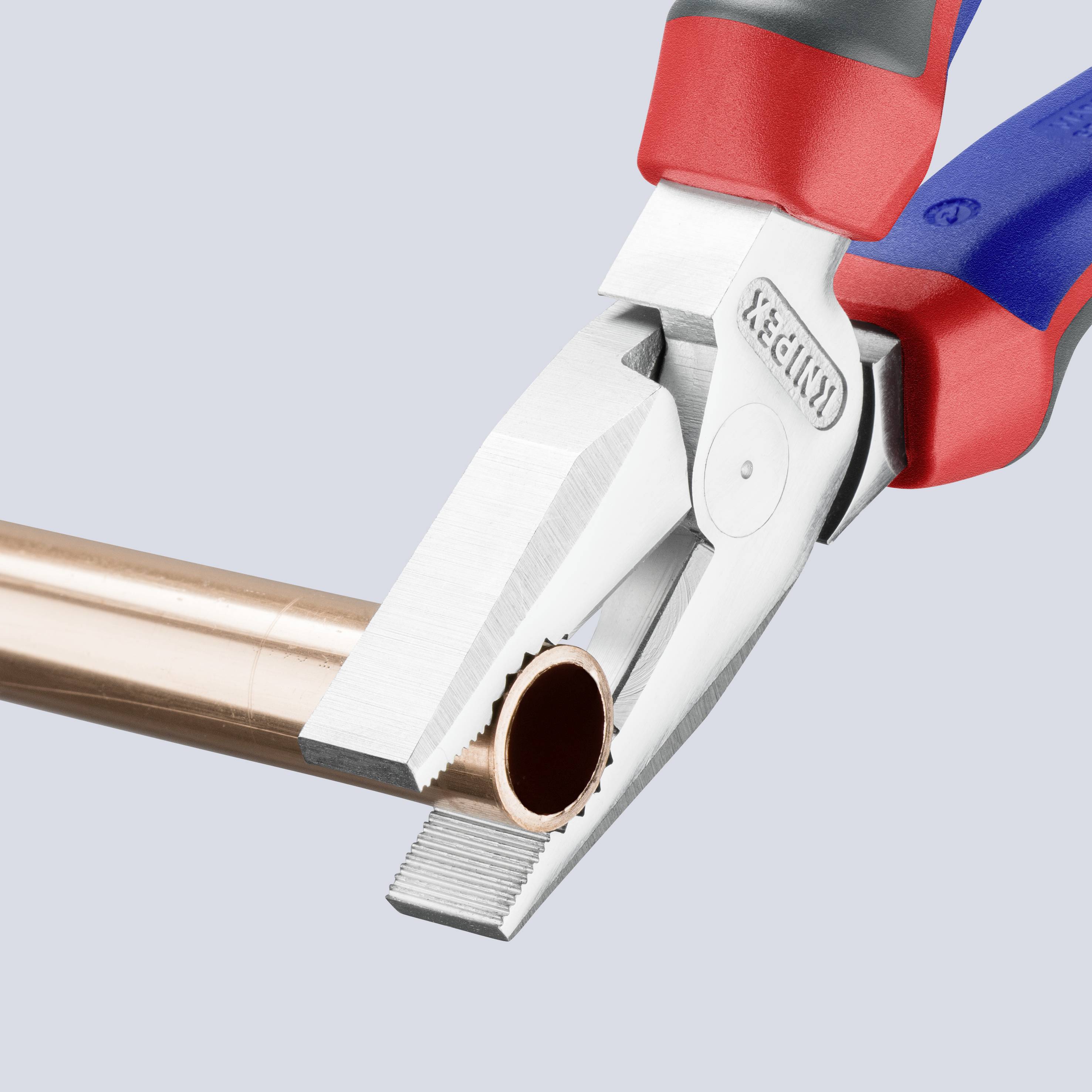 A pipe cutter cuts copper piping. The tool is red and blue with a silicone coating for better grip. Ideal for plumbing and DIY work.