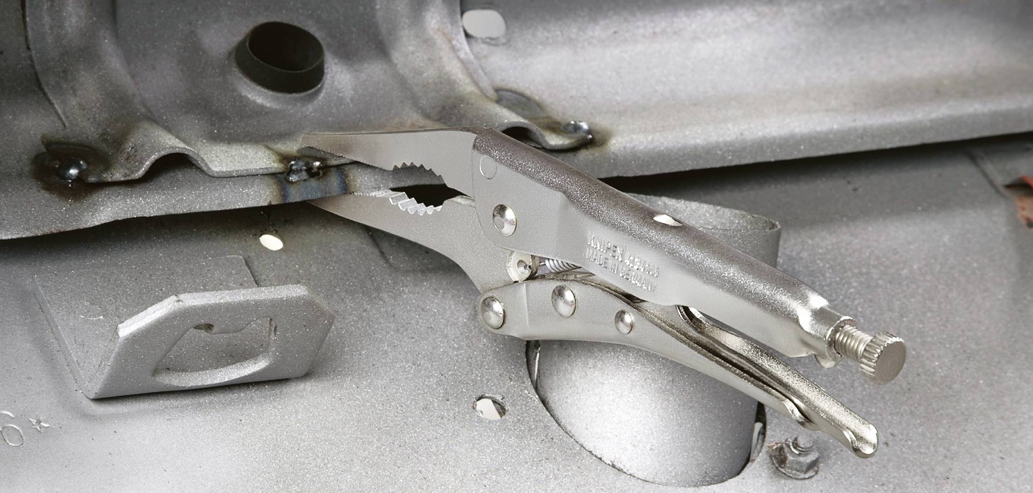 A silver locking pliers grips a metal sheet. It is often used to hold objects securely in place.
