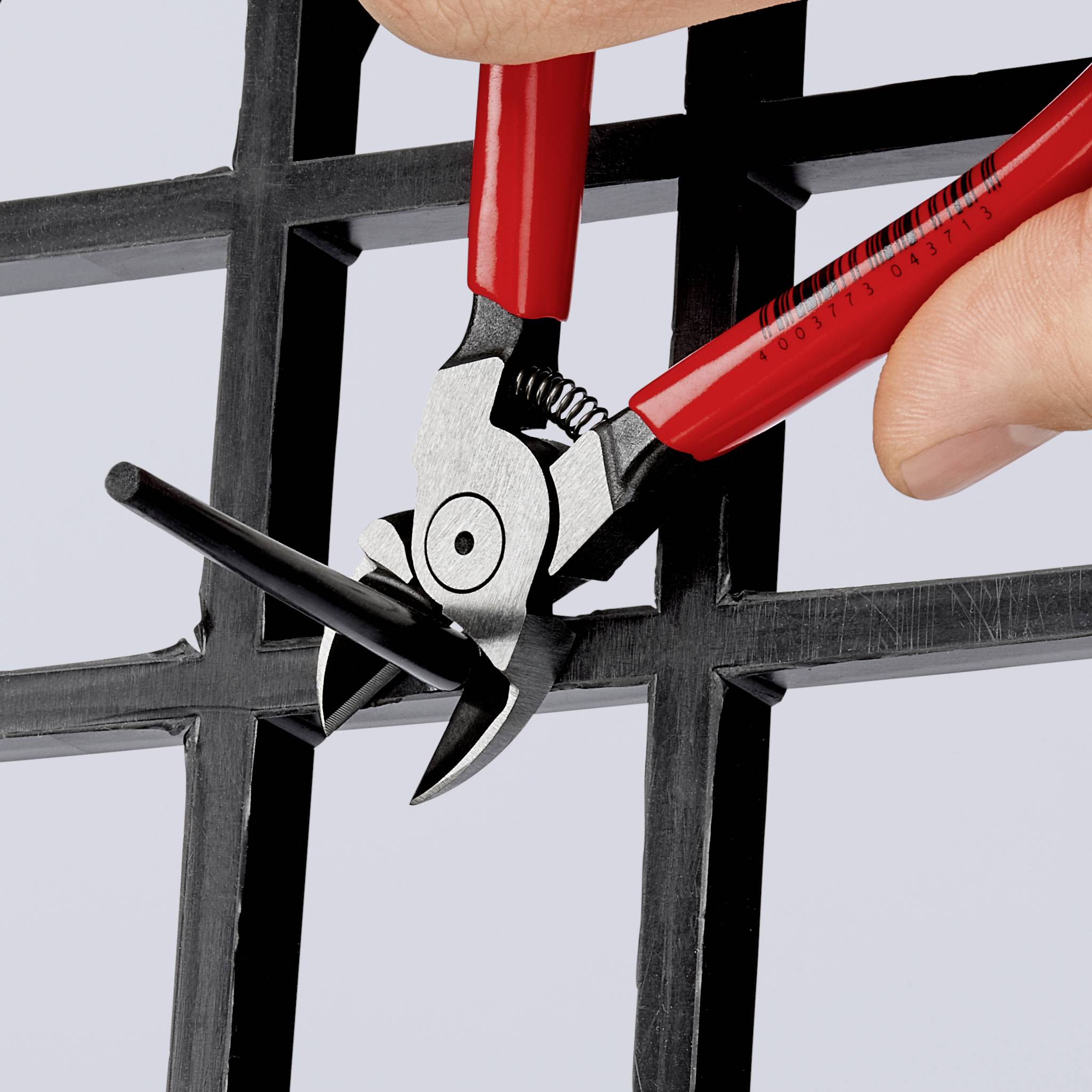 A red pair of pliers cuts through a wire fence. A hand holds the pliers while cutting through the wire with precision.
