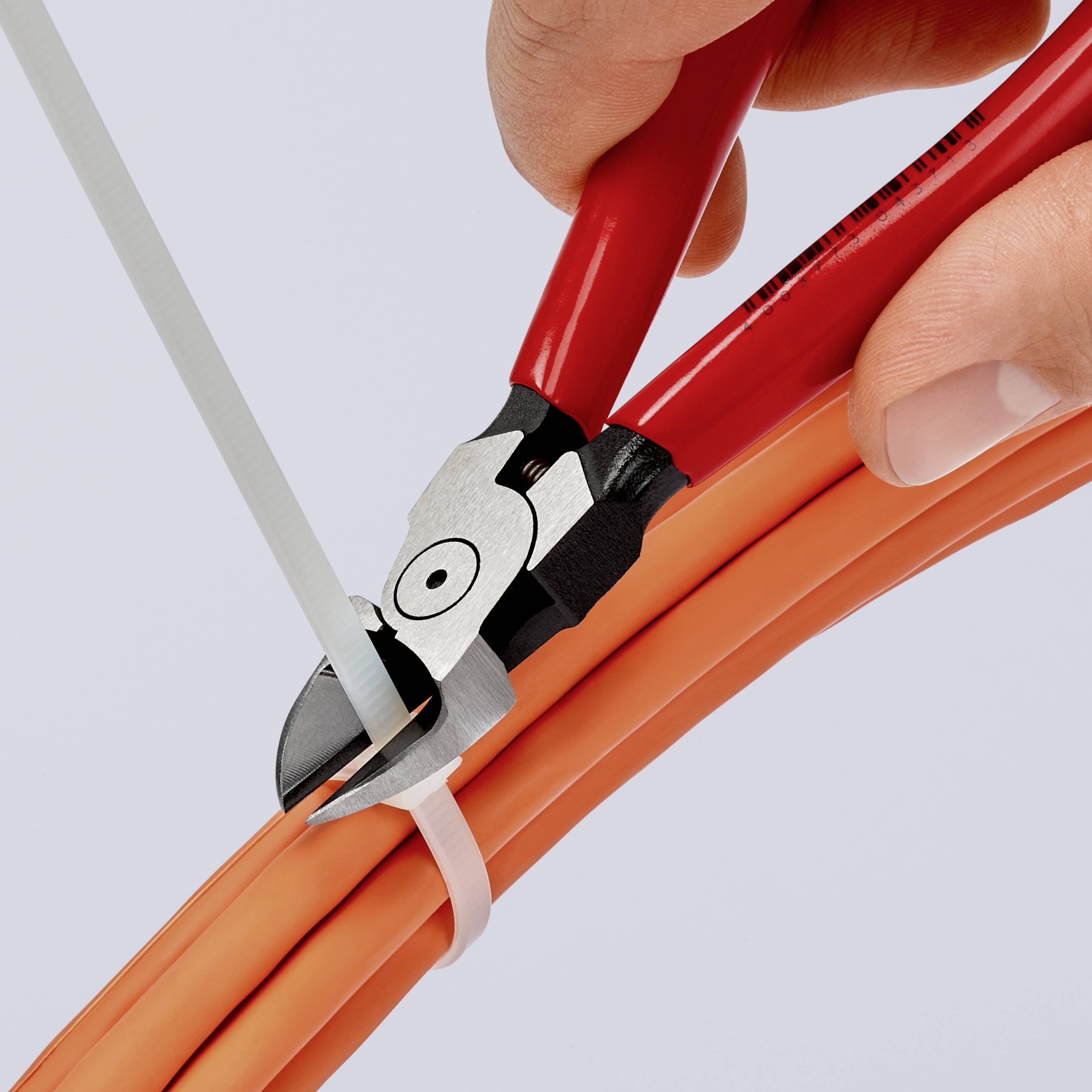 A hand holds a side cutter and is cutting a white cable tie that is holding together several orange cables.