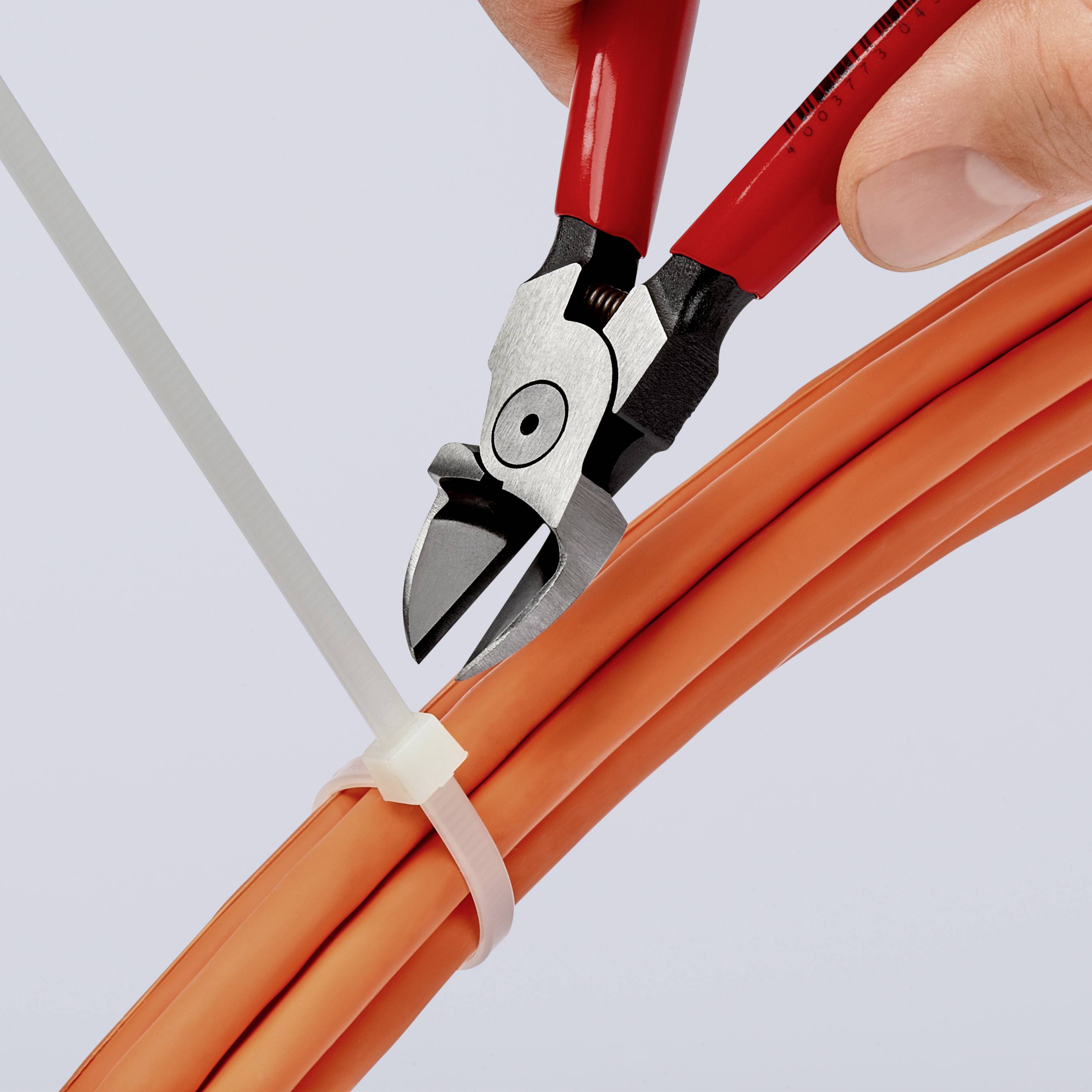 A hand is cutting a white cable tie with a red pair of pliers, which is wrapped around several orange cables.