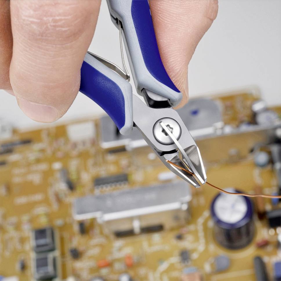 A person is holding a blue wire-cutting pliers and cutting a wire on a circuit board. The background shows electronic components.