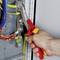A hand is holding a red pair of pliers and working on an electrical assembly with copper wires and coloured cables on a metal plate.