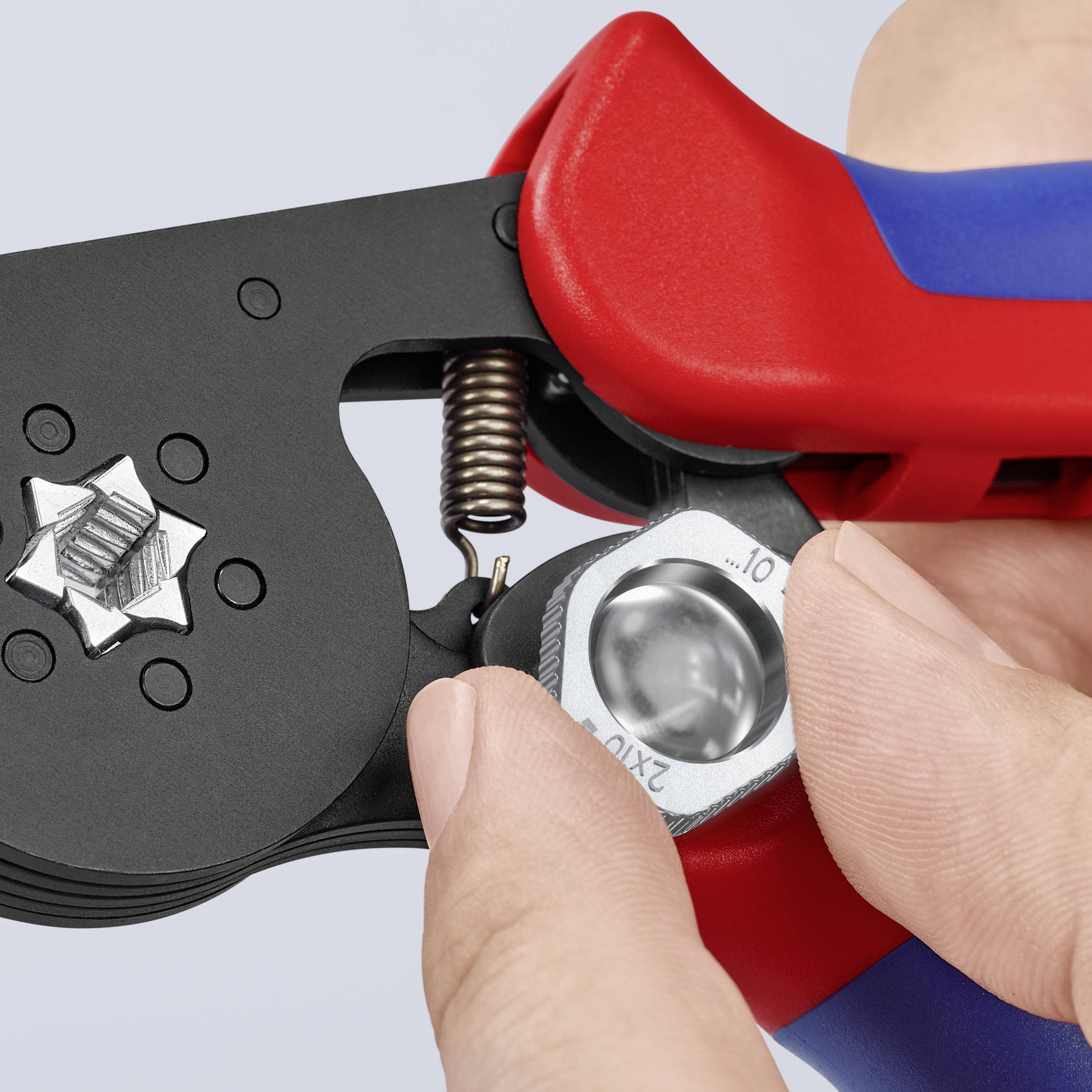 A person is using a red and blue crimping tool to press a metal piece with a clip. The hand and tool are visible.