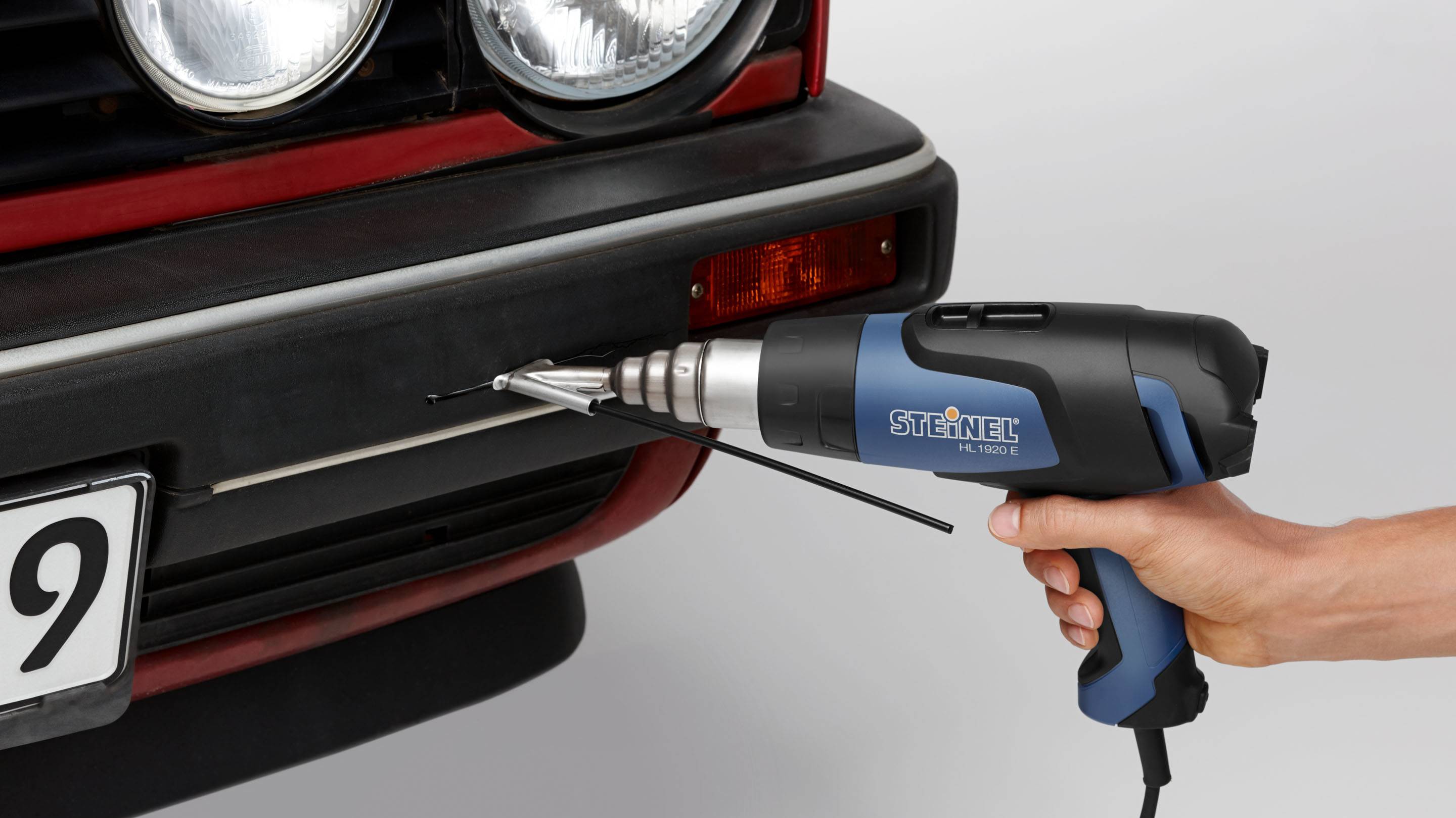 A person is holding a hot air blower aimed at a car's bumper.
