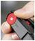A person's fingers adjust a red plastic dial with plus and minus symbols, attached to a black device, indicating tension or calibration.
