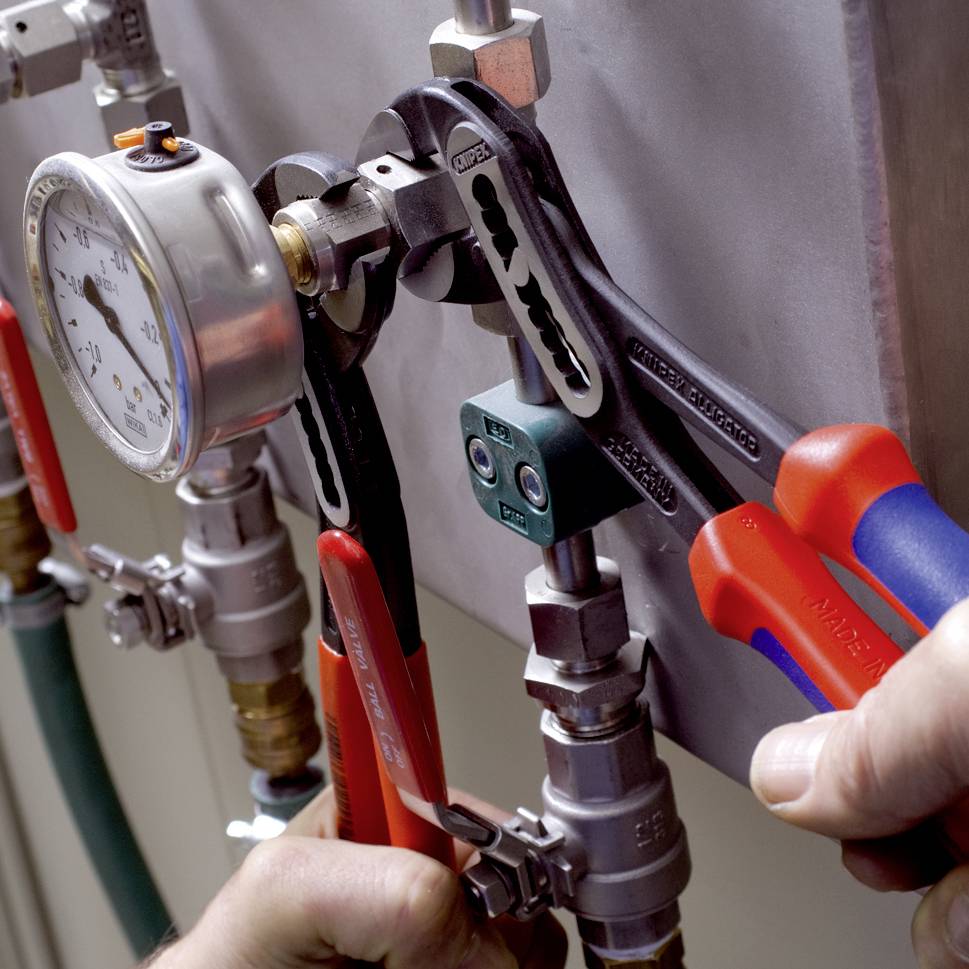 A person is repairing a pipeline using two adjustable wrench spanners on the connection joints. A pressure gauge is displaying a reading.
