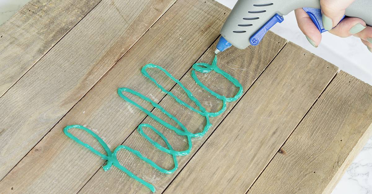 A wooden plank-covered table, on which the word 'hello' is written in green using a hot glue gun.