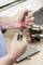 Hands using a screwdriver with an interchangeable bit, on a workbench with metal tools in the background.
