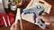 'Person is sticking wooden pieces to a wooden table using a hot glue gun with adhesive and a red cloth'