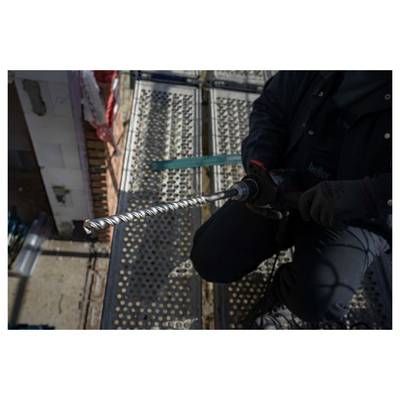 Worker using a power drill with a long bit on a metal platform or scaffolding, viewed from above.<br>