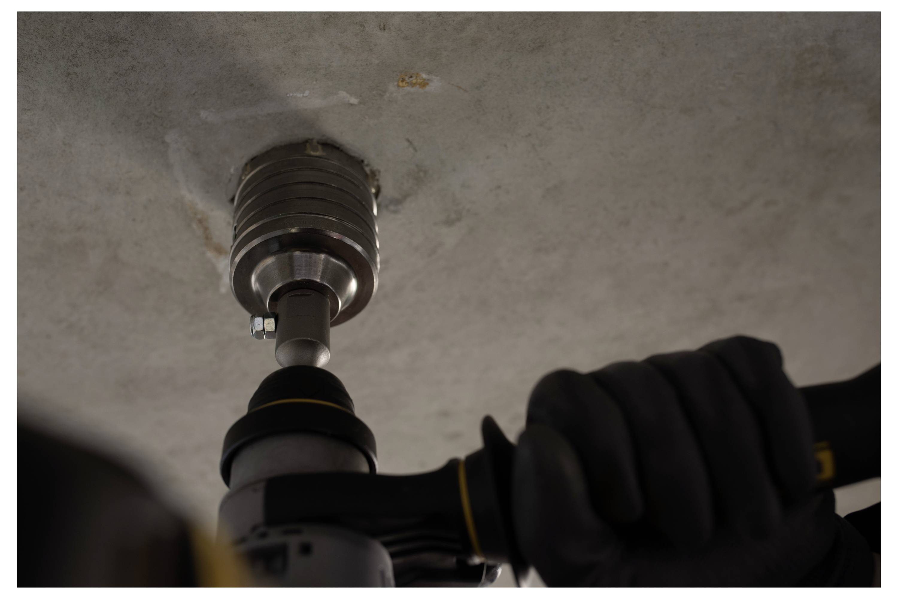 Gloved worker uses a power drill to install a ceiling-mounted light fixture or anchor into concrete.