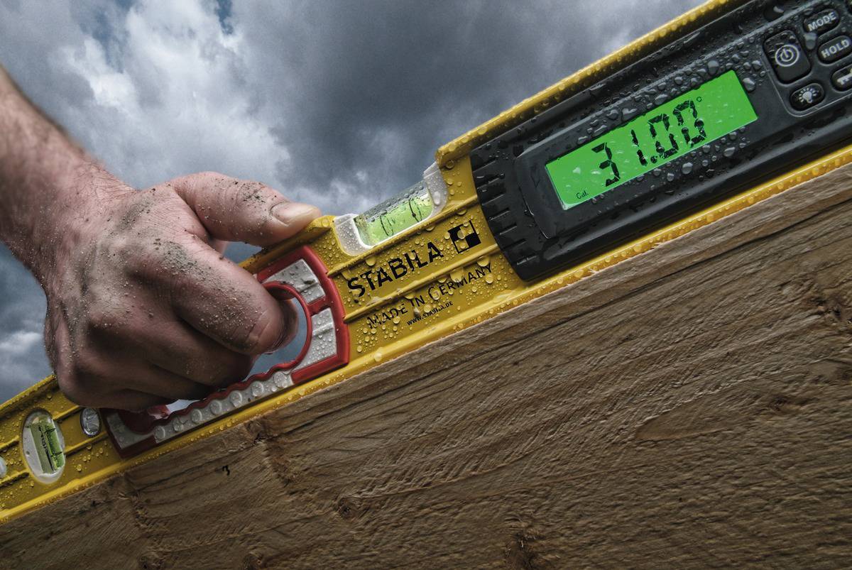 A hand is holding a yellow spirit level with a digital display reading -31.00, over a wooden beam, against a cloudy sky.