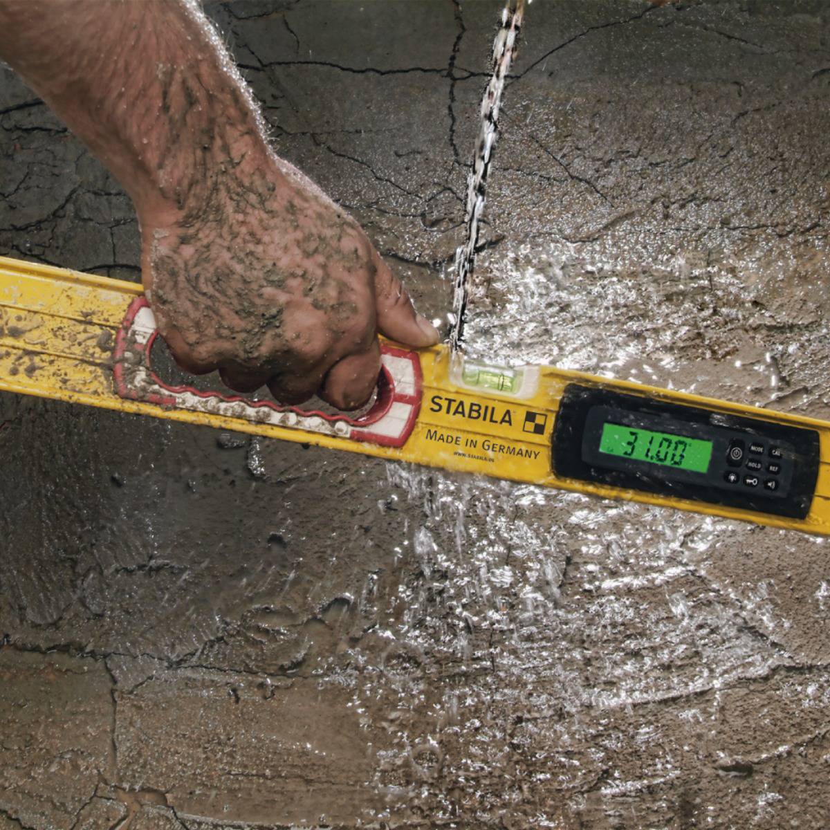 A construction worker checks the horizontal alignment of a wet, concreted surface using a spirit level.