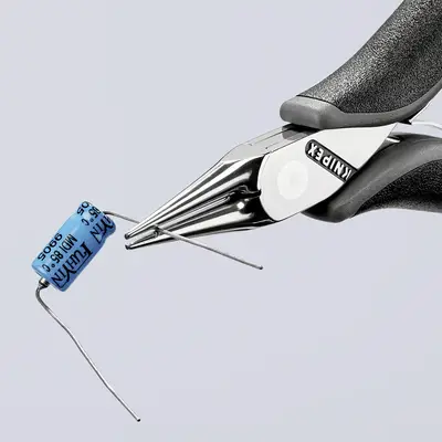 A pair of pliers is holding a blue electrolytic capacitor. The pliers are silver with black handles, and the brand is visible.