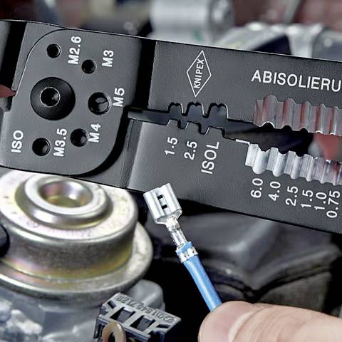 A hand uses a black wire stripper tool to strip a blue wire. The tool has various size markings for different wire gauges.