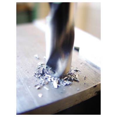 Close-up of a drill bit boring into a metal block, with curled metal shavings around the hole.