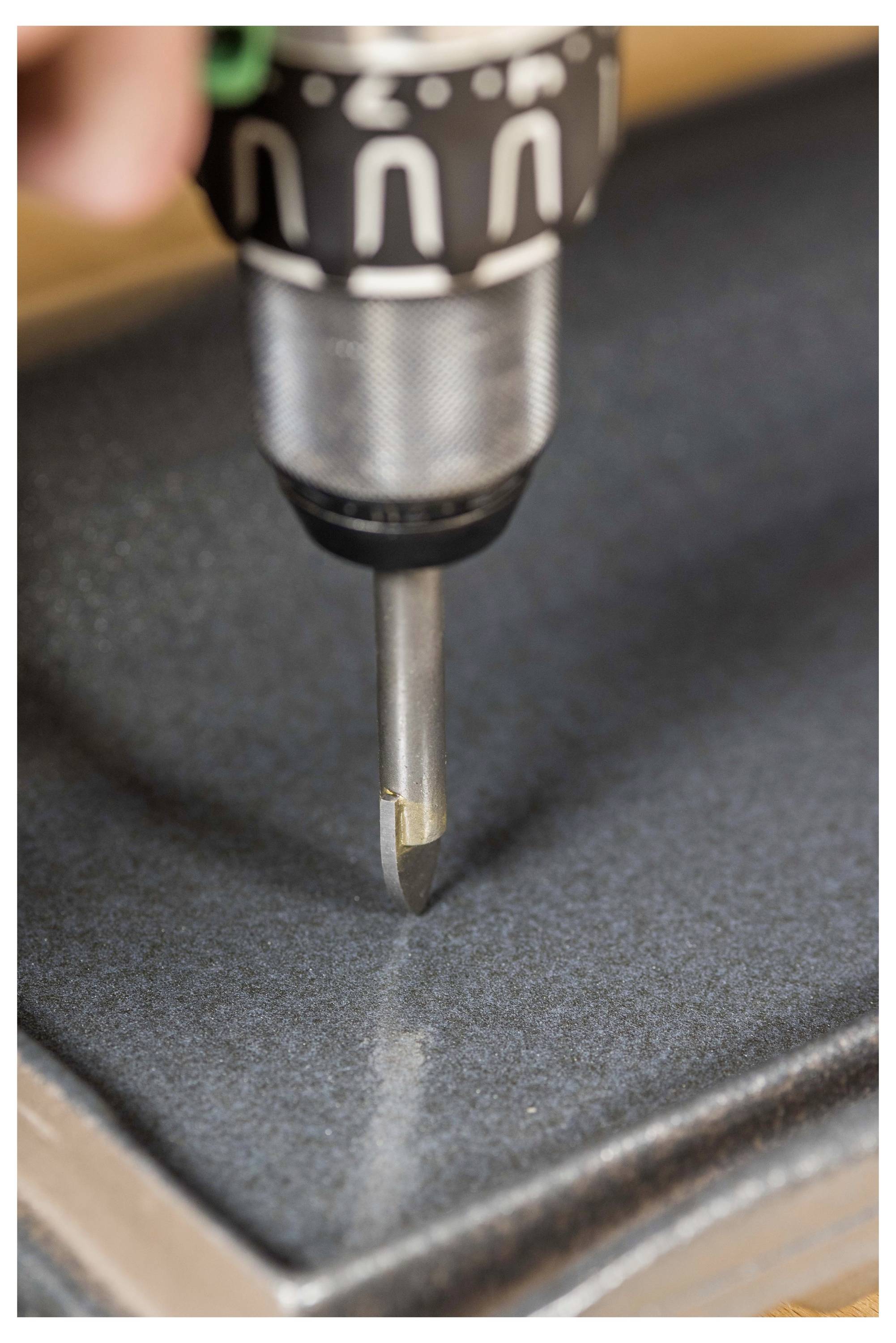 Close-up of a drill bit poised against a dark metal surface, suggesting drilling or fastening work.