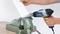 A person is holding a heat gun and working on a white sheet metal that is clamped in a vice.