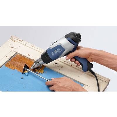 A person is using a blue heat gun to remove paint from an old wooden door frame.