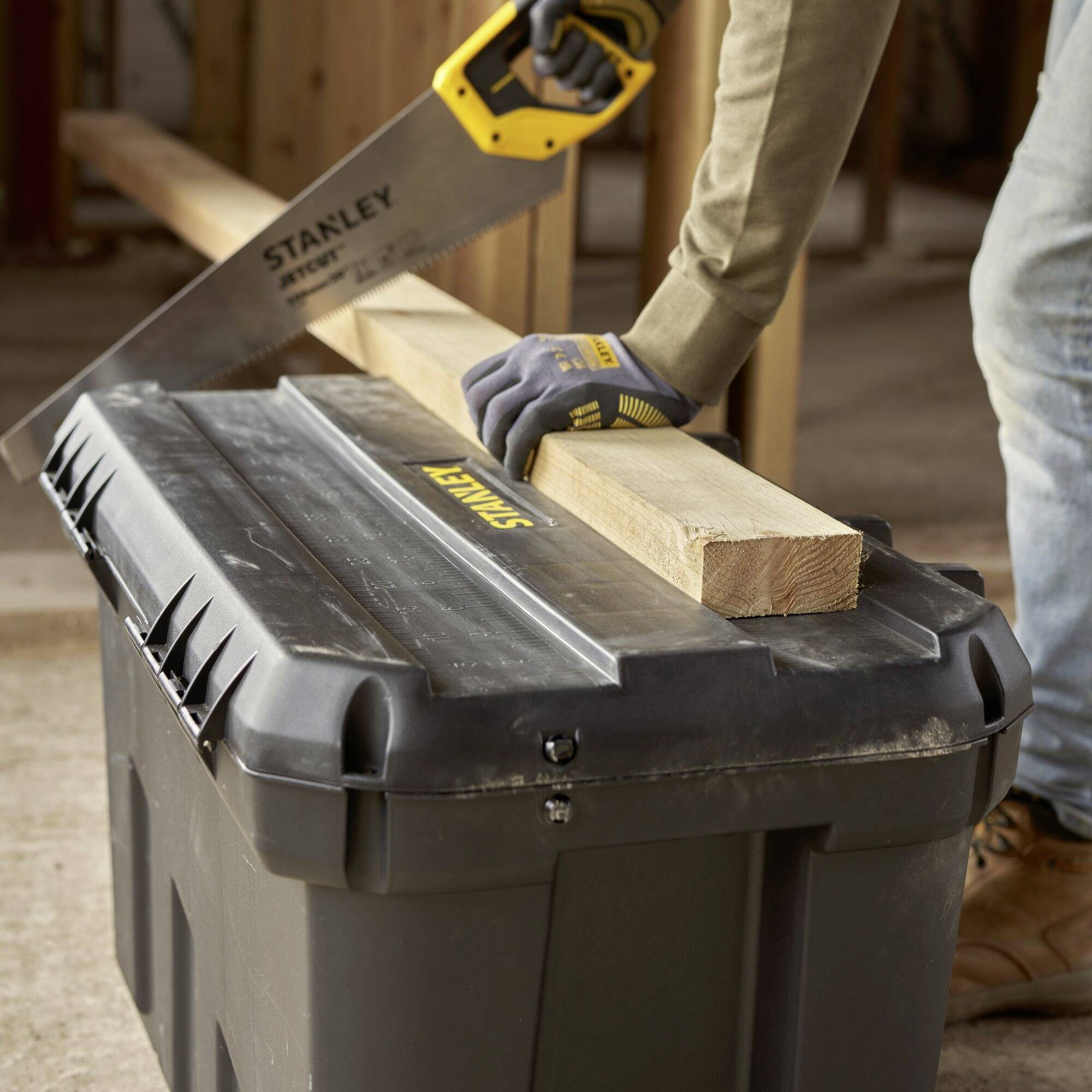 A person is sawing a piece of wood with a handsaw on a black toolbox.