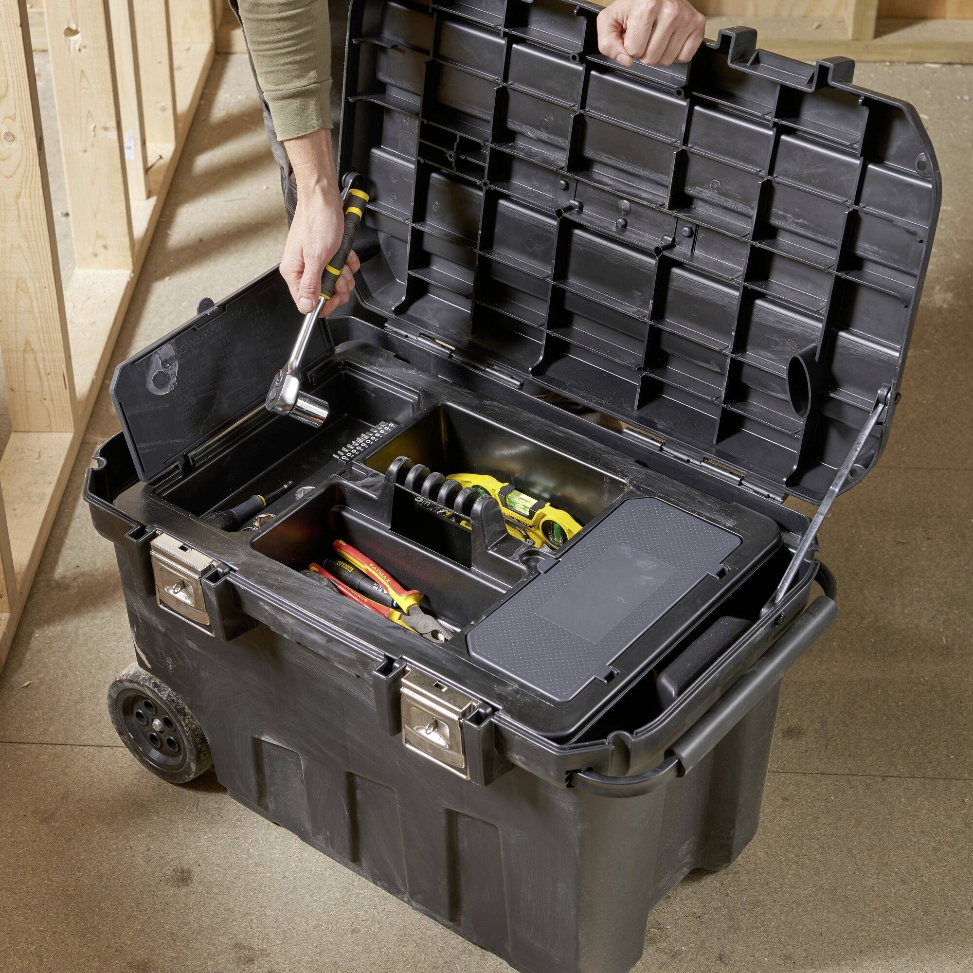 An open toolbox on wheels, filled with various tools such as screwdrivers and spanners. A hand reaches for a screwdriver.