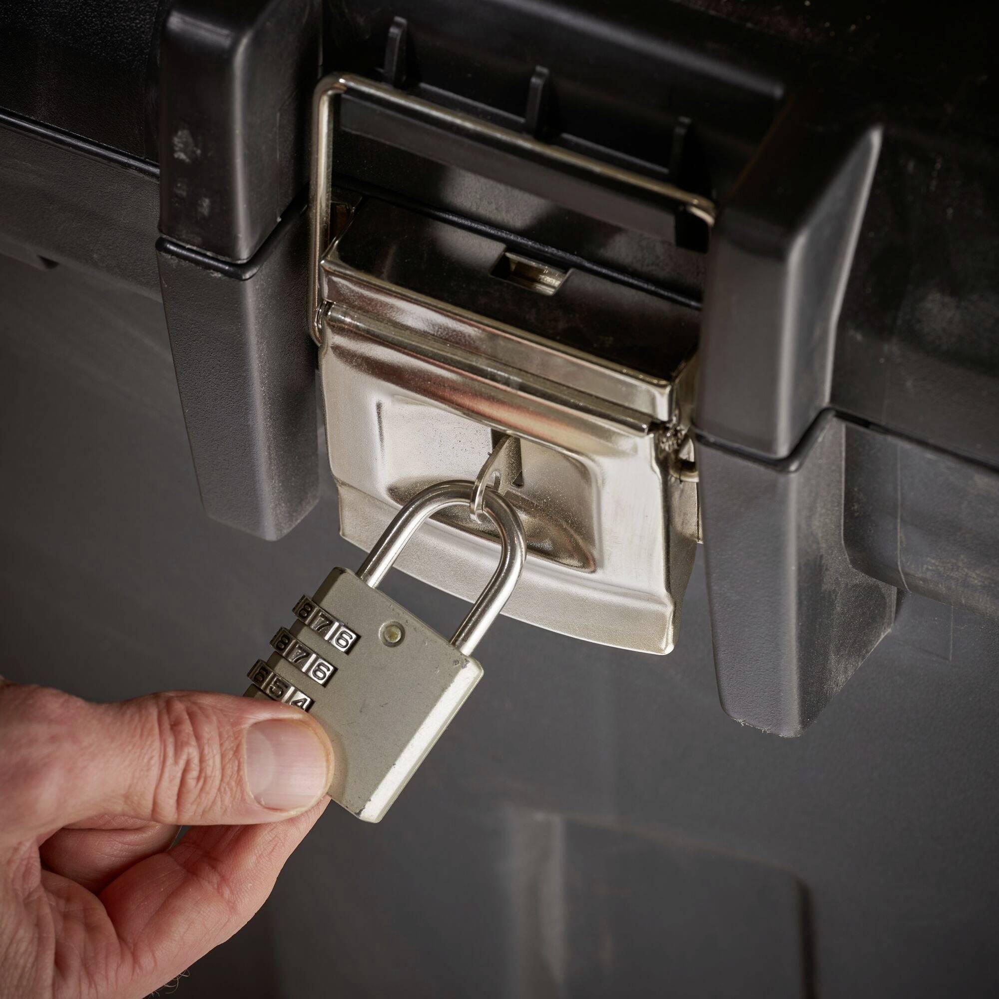 A hand locks a padlock on a metal box. The lock displays four number dials used to secure the box.