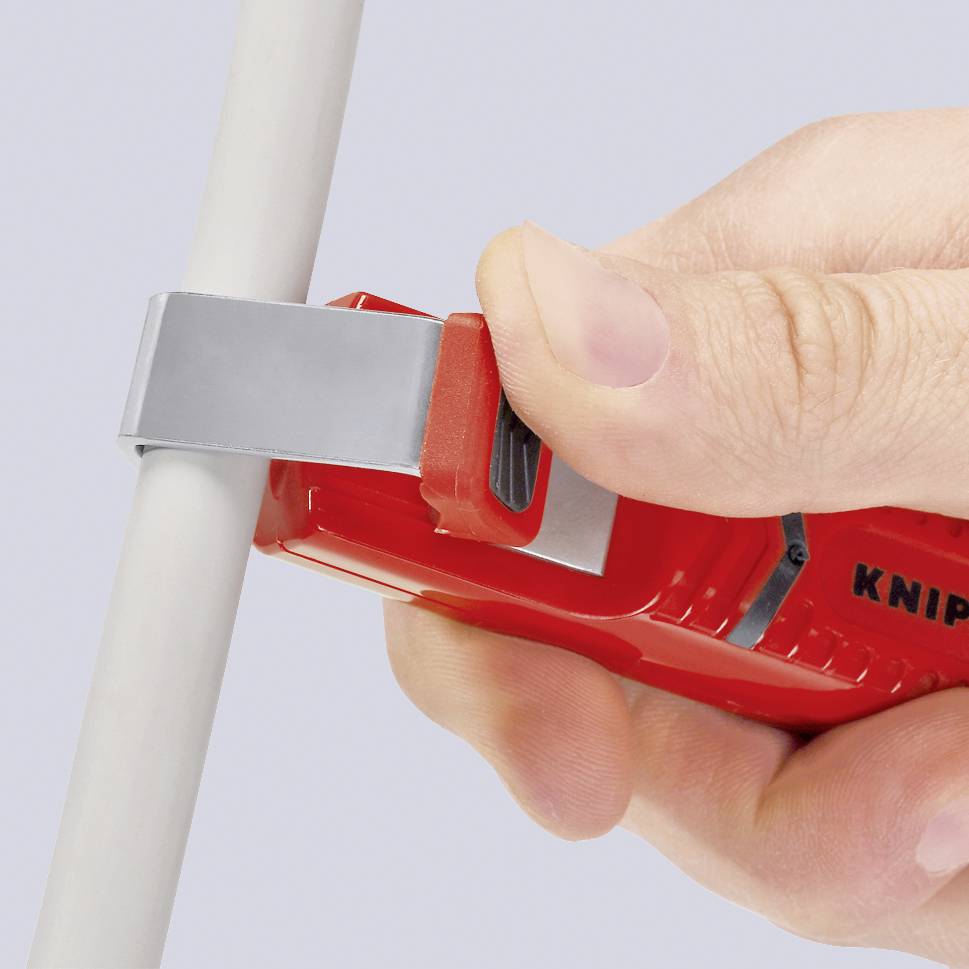 A hand is holding a red pipe cutter, which firmly grips a white pipe.