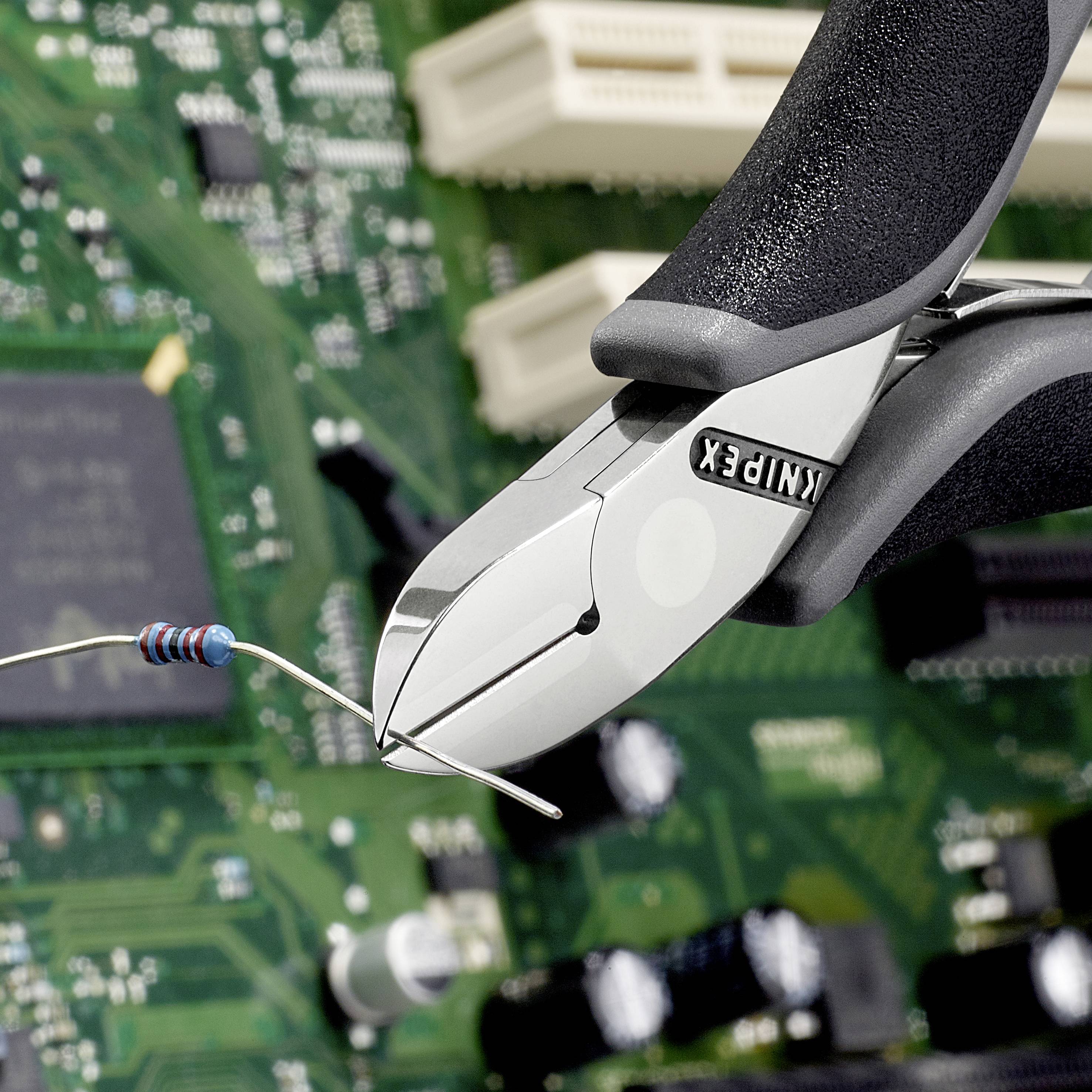 A wire cutter is cutting a blue resistor over a green circuit board with visible electronics.