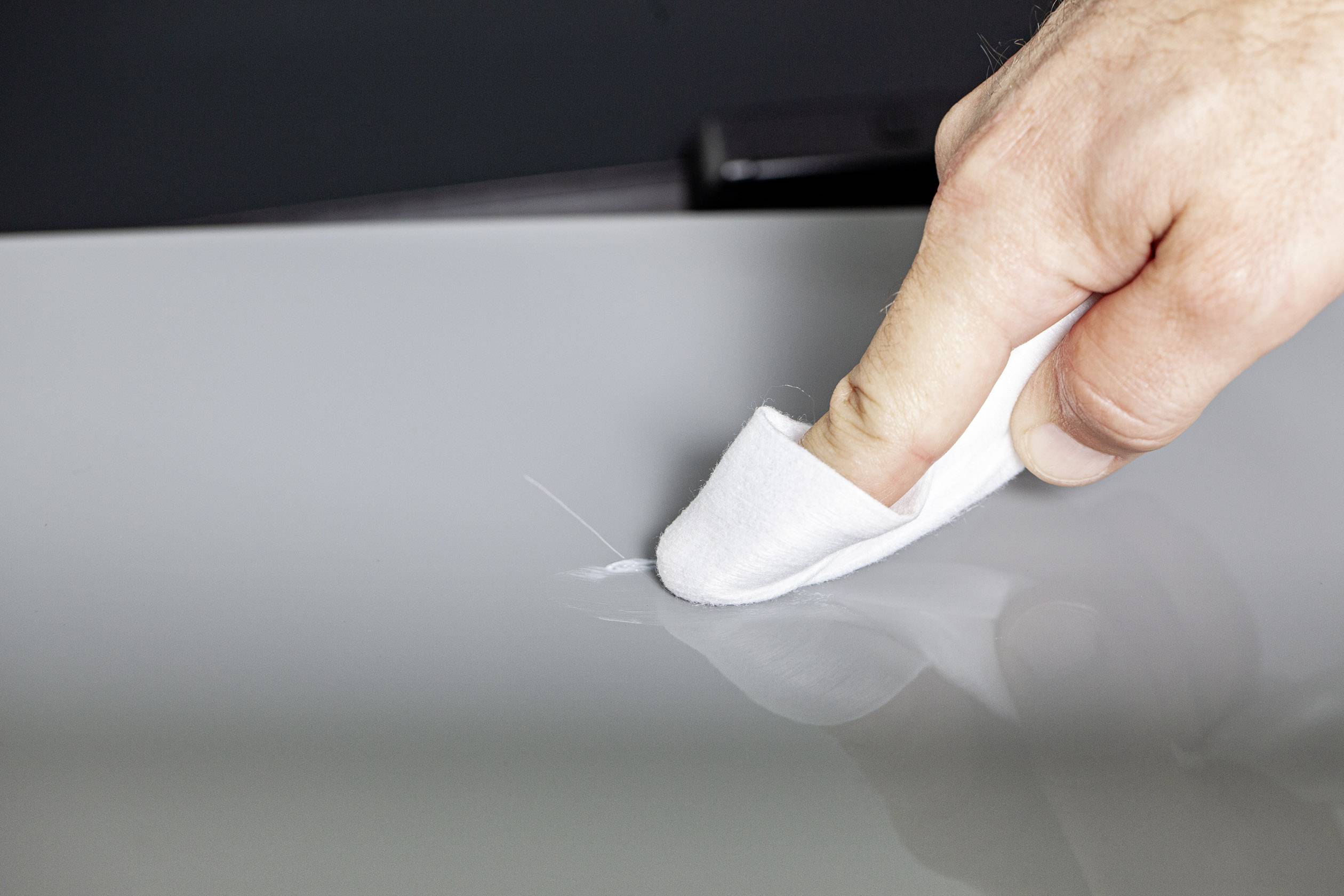 A hand wipes a grey, smooth surface with a white cloth, removing dust.