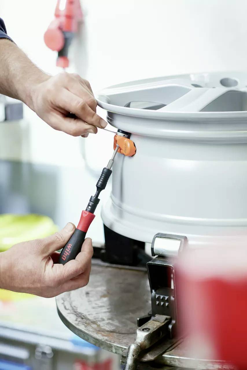 A person is using a tool to mount a sensor on a bright alloy wheel. The focus is on precise manual work.
