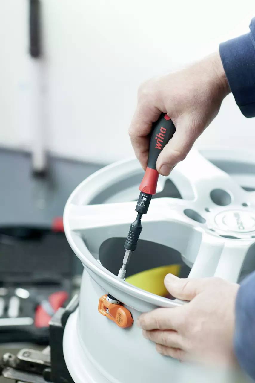 A person tightens a screw on a silver car wheel with a screwdriver.