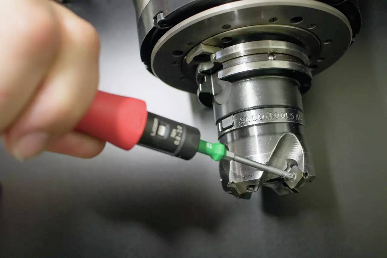 A hand is holding a screwdriver whilst working on a metal device. The device has rotating parts and has an industrial appearance.