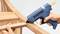 A person is using a blue hot glue gun to stick two pieces of wood together.