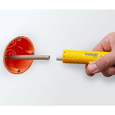 A hand uses a yellow wire stripping tool to strip insulation from a cable emerging from an orange wall socket opening.