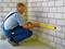 A man in work attire is using a spirit level to check the alignment of a brick wall in an unfinished room.