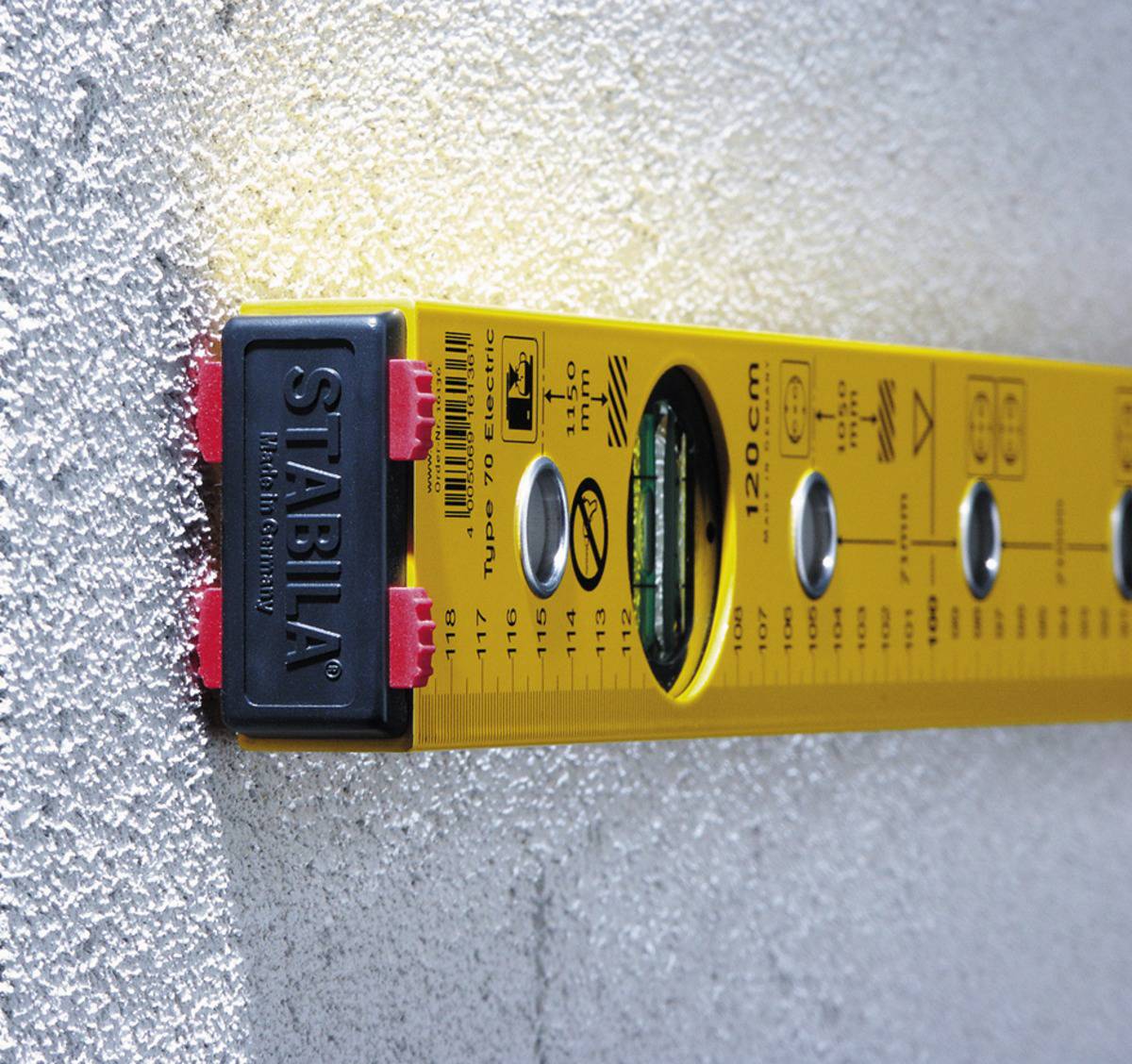 A yellow spirit level is resting against a rough, grey wall, indicating that its position is horizontal.