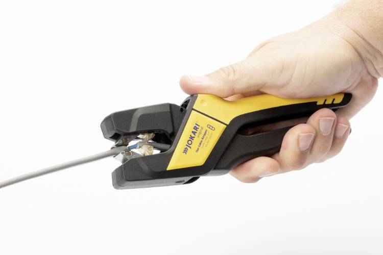 A hand is holding a wire stripping tool that is working on a cable. The tool is black and yellow and is firmly closed around the cable.