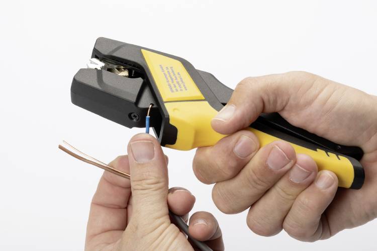 A person is holding a wire stripping tool and removing the insulation from a copper cable.