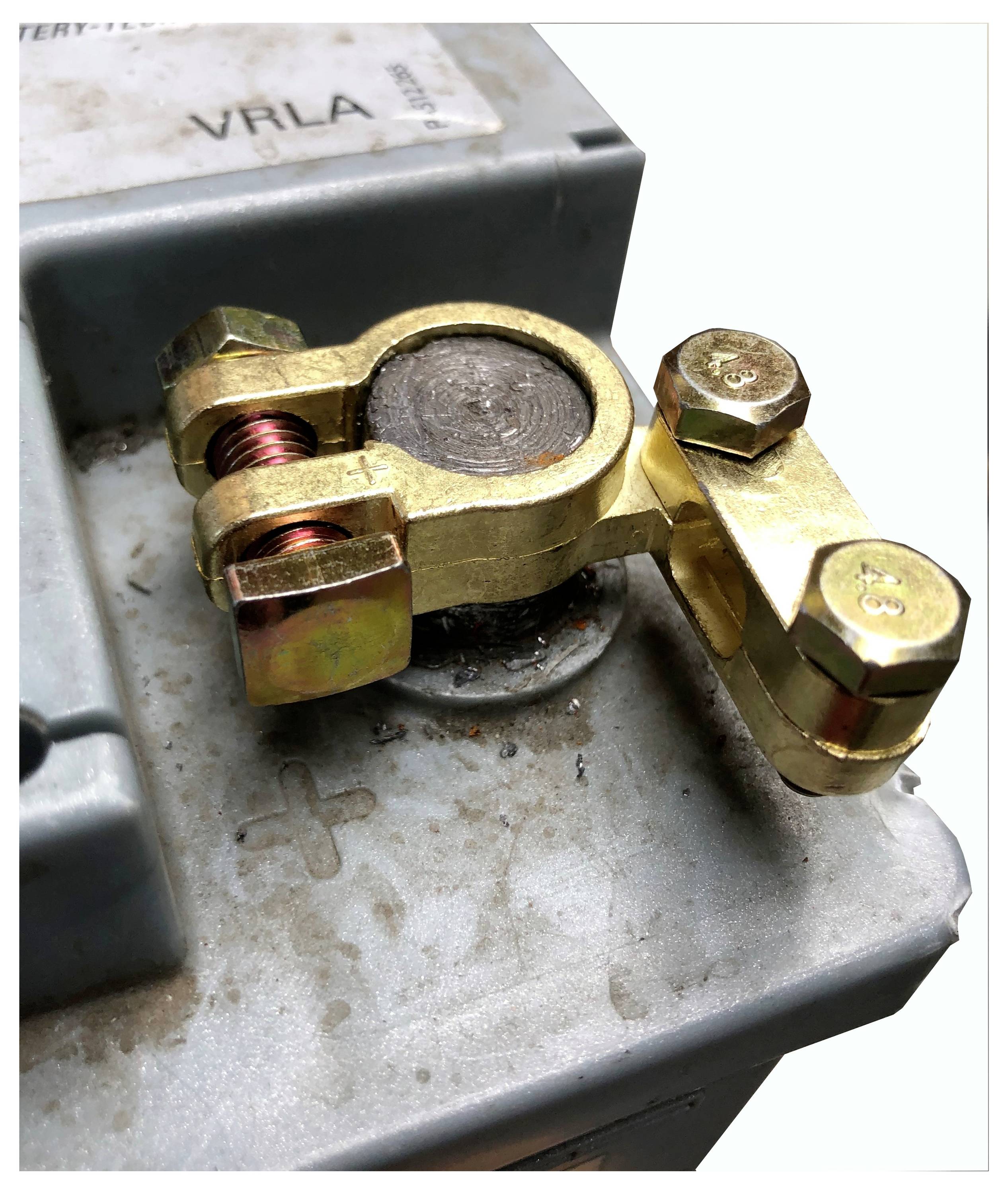 A close-up of a car battery terminal with a newly installed brass connector. The '+' symbol is visible on the battery, indicating the positive terminal.