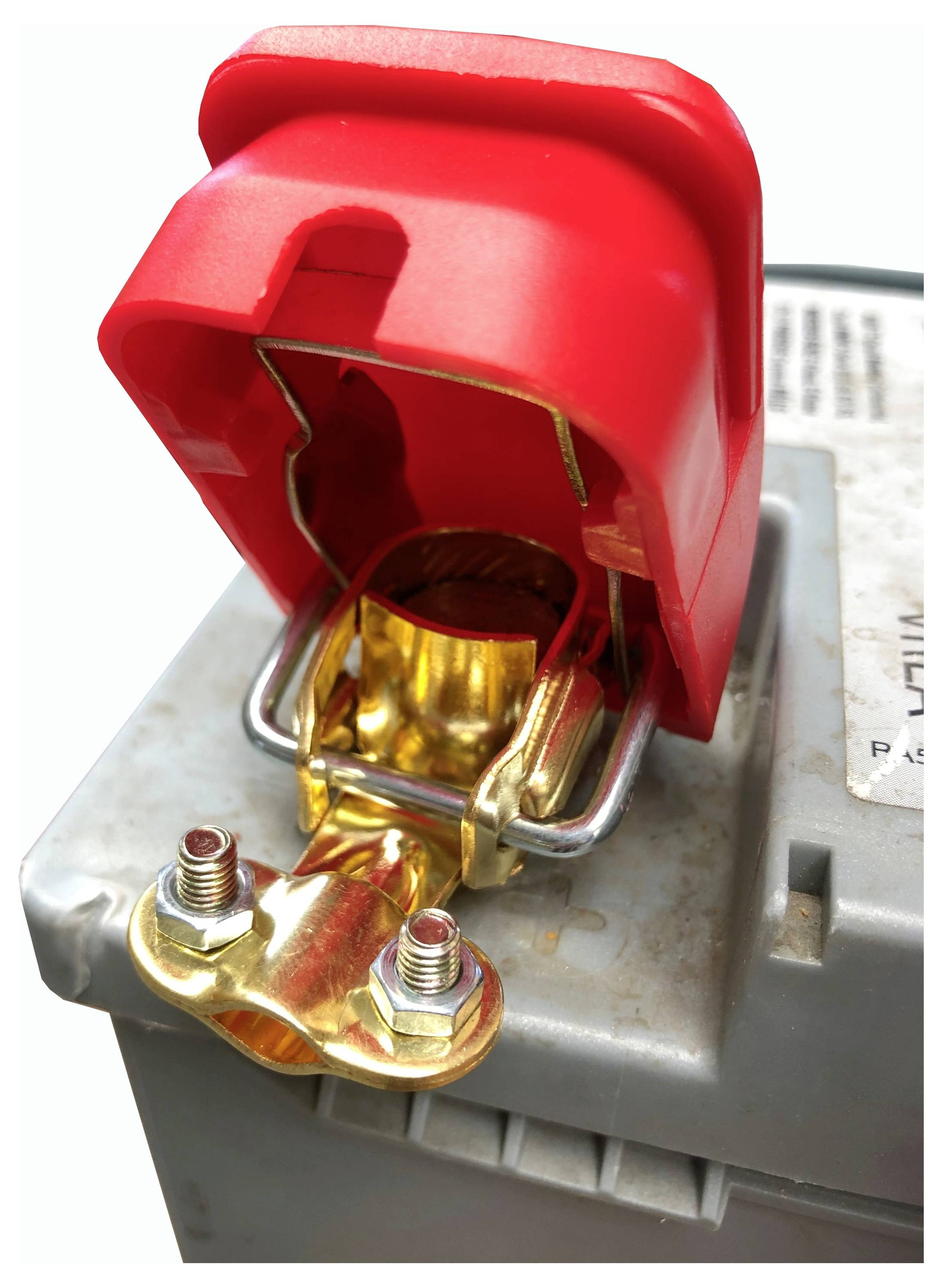 A close-up of a battery terminal with a bright red protective cap, metal clamps, and two bolts. The terminal is attached to a gray battery.