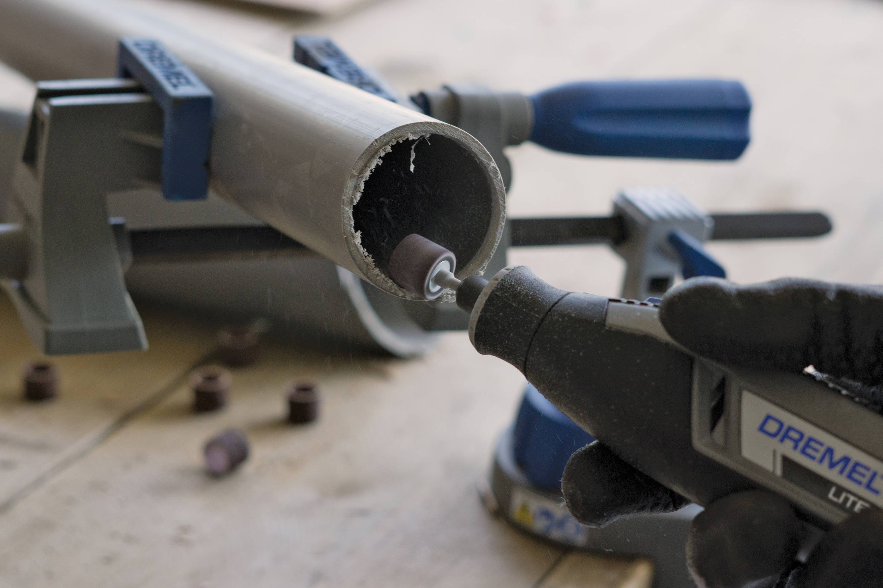 A person is grinding the edge of a pipe with a rotating tool. The pipe is secured in a vice.
