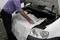 A person is spreading a protective blanket over the engine compartment of a car. The bonnet is open.