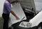 A man is placing an insulating blanket in the engine compartment of a car, likely to protect the engine from cold.