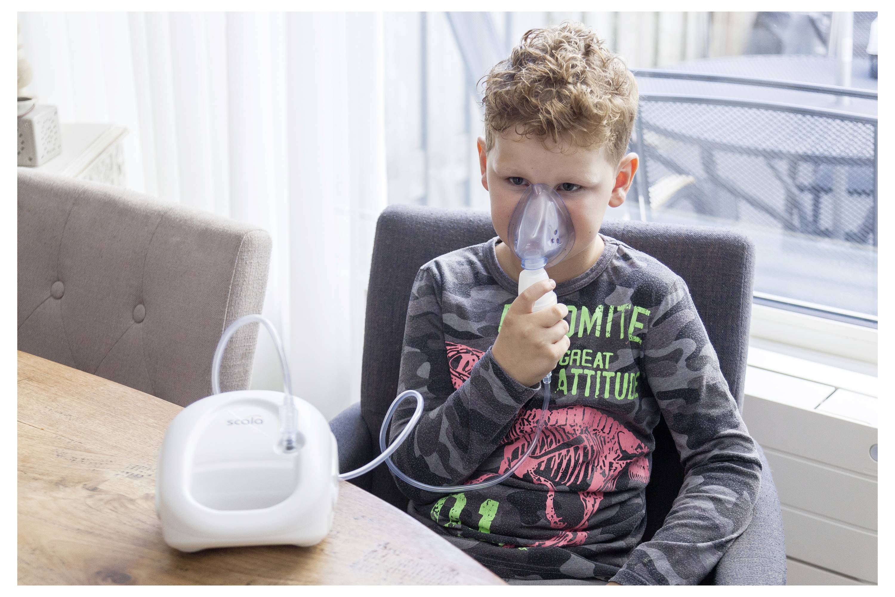 A child sits at a table using a nebulizer with a face mask, receiving a breathing treatment.