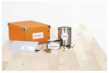 On a wooden table stand three containers: An orange box labelled 'Decoration', a silver container marked 'Coffee', and a biscuit tin.