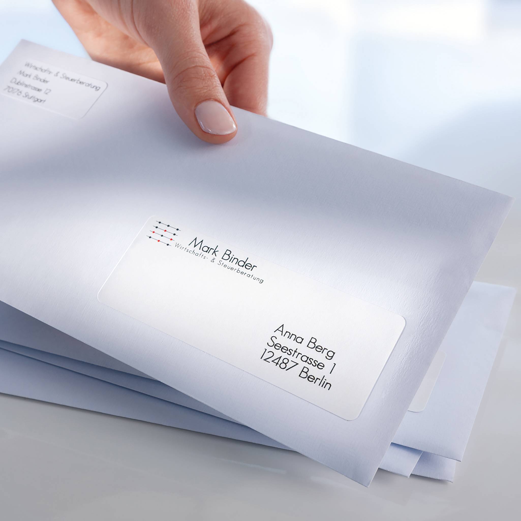 A hand is holding an envelope addressed to 'Mark Binder' with an address in Berlin. The envelope is sealed and ready to be posted.