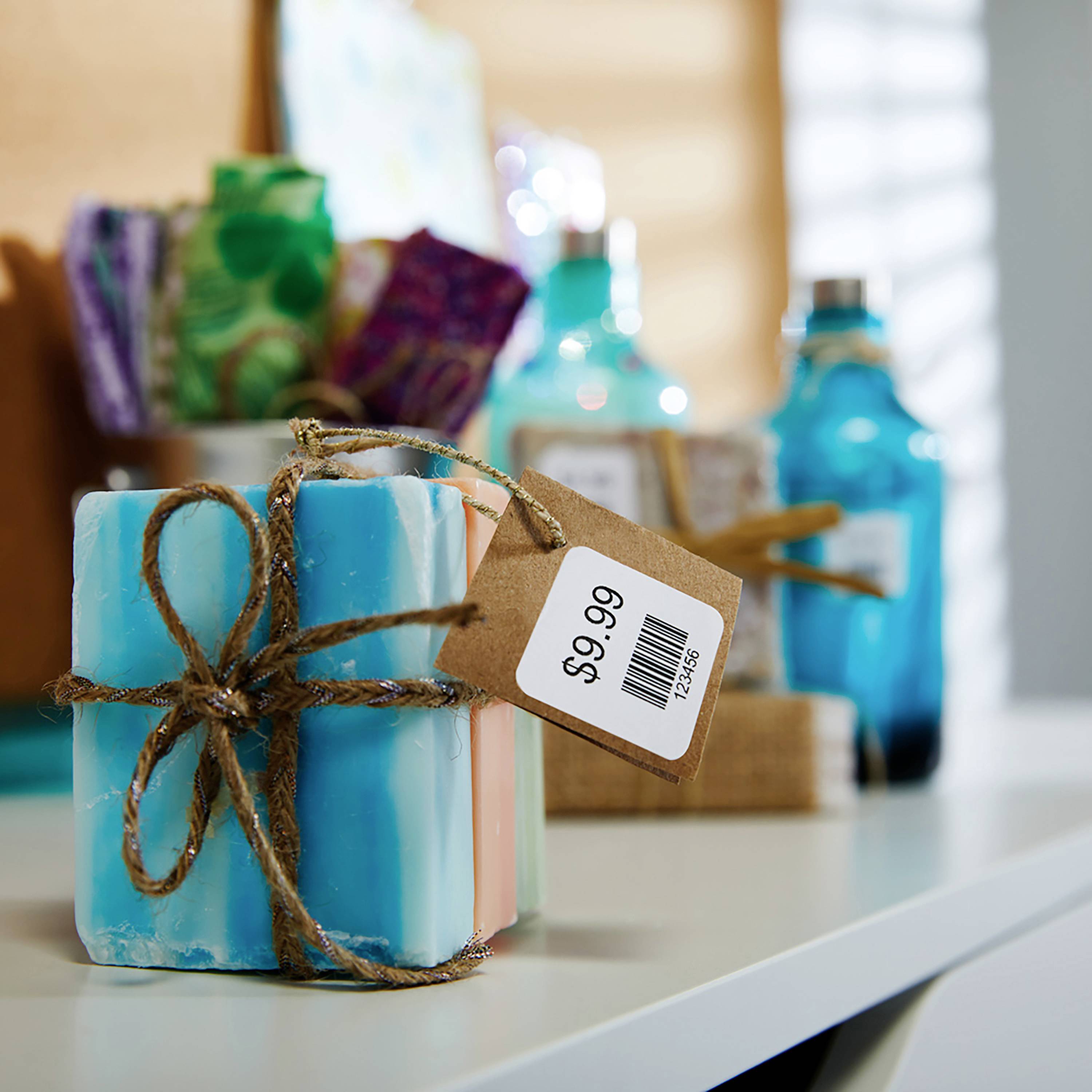 A blue, handmade soap bar, tied with string and featuring a price tag of £9.99, sits in the foreground on a shelf.