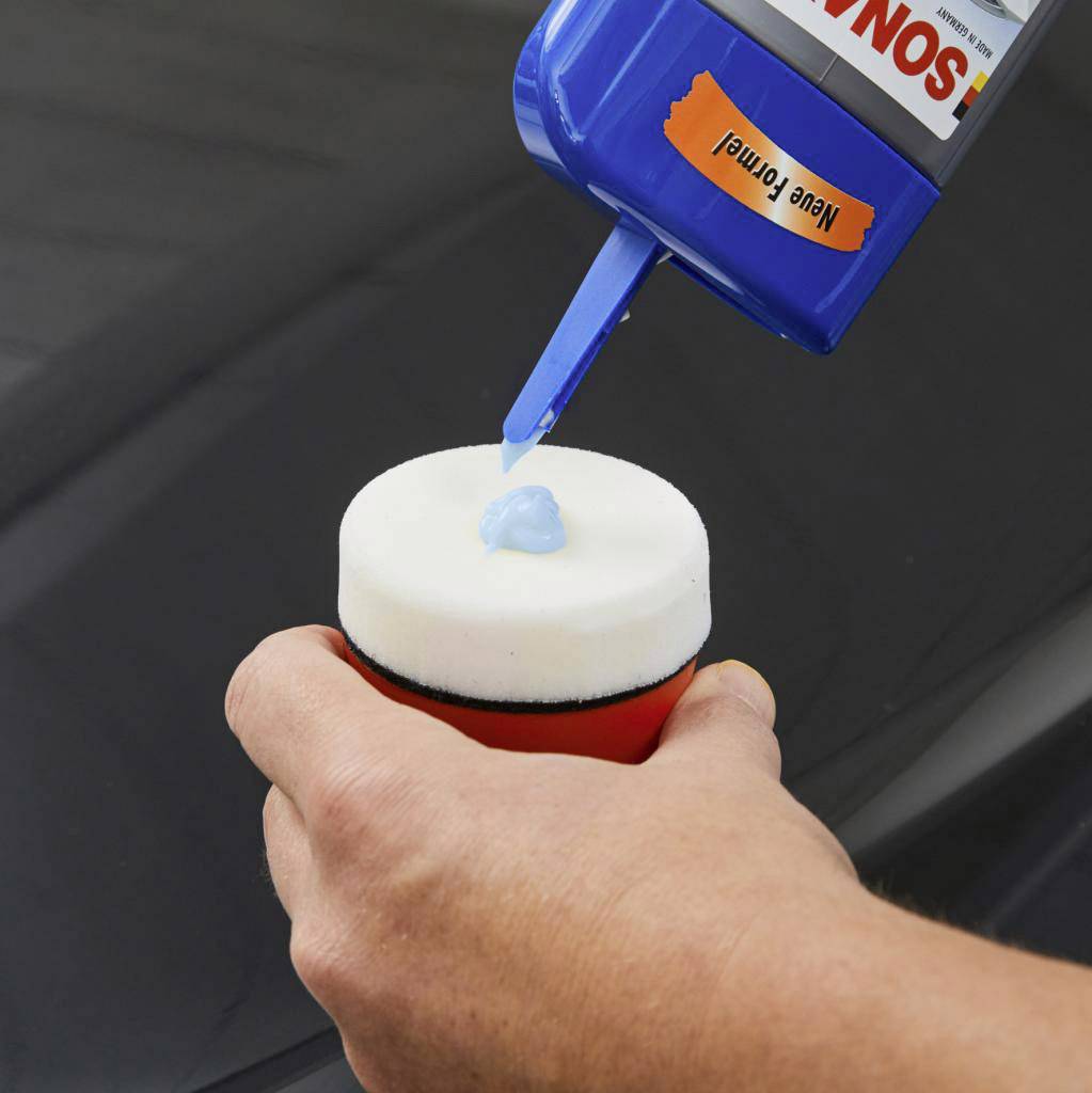 A hand is holding a polishing sponge, with blue polish being squeezed onto it from a tube.