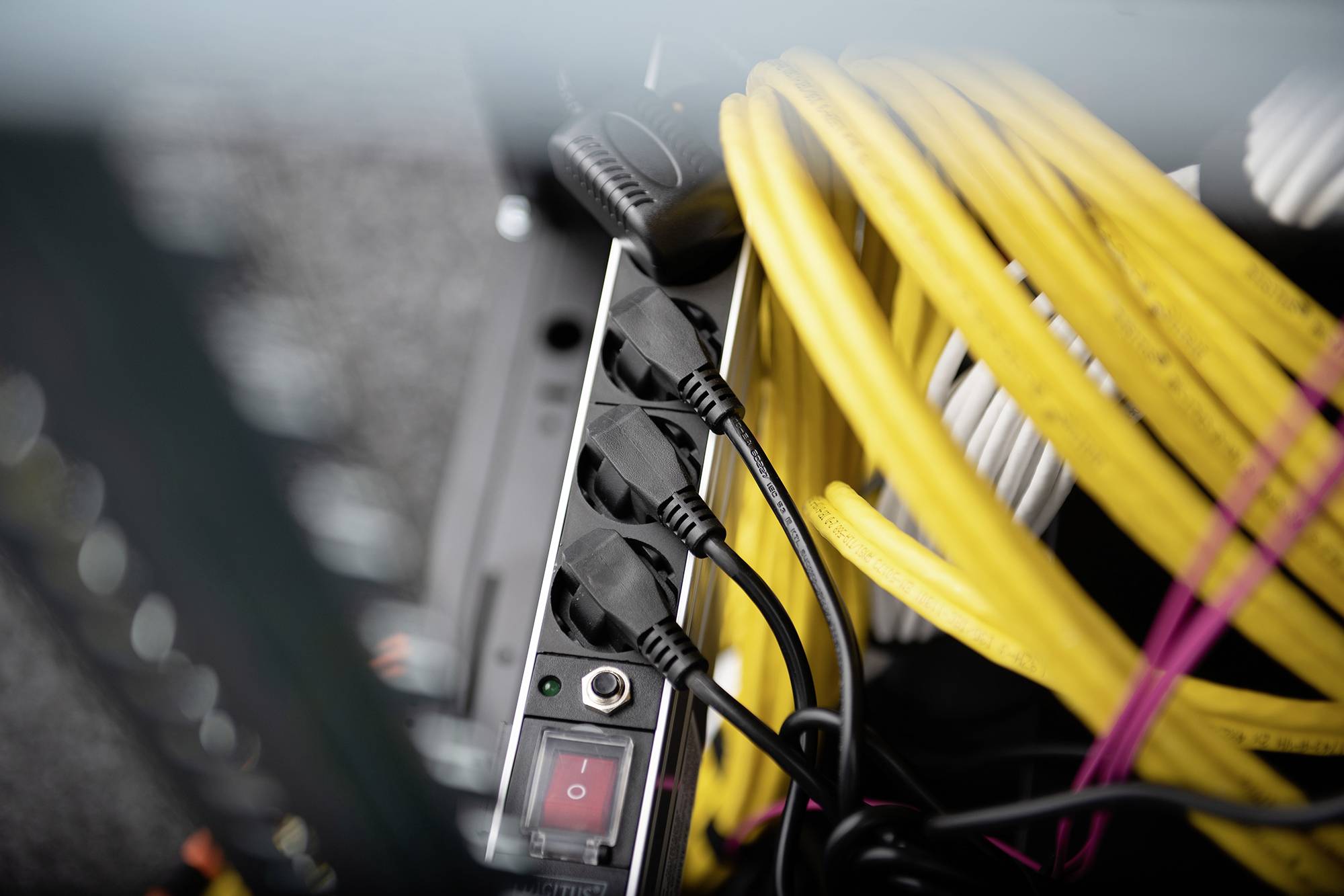 A black multi-socket adaptor with four connected cables next to yellow cables, likely situated in a technical or server room.